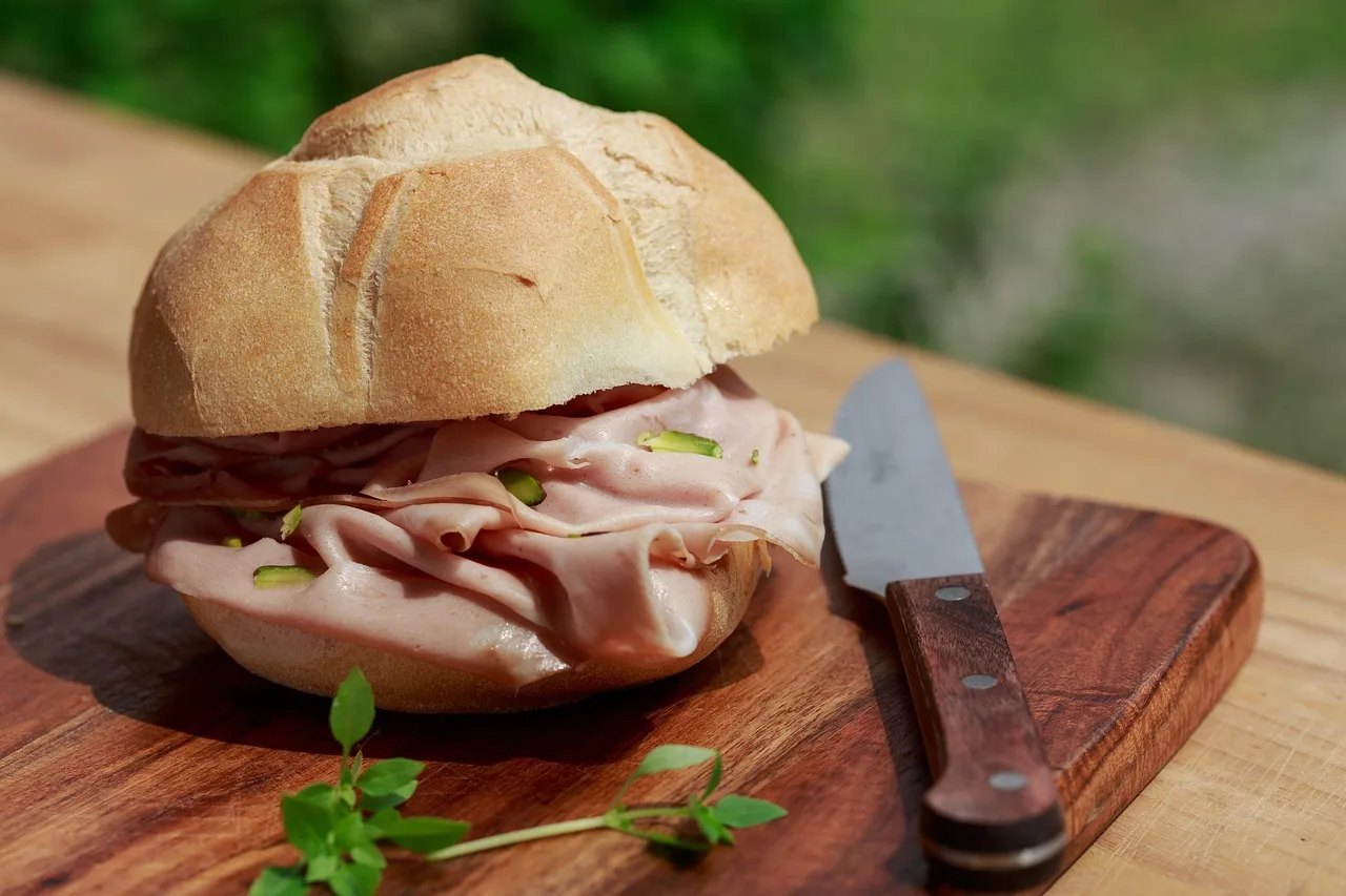 Fette di mortadella su un tagliere, con un piatto di insalata sullo sfondo.